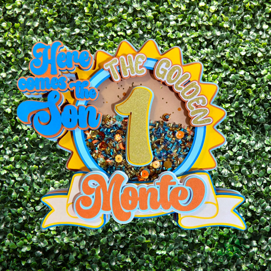 Decorative birthday sign with 'Here comes the Sun, The Golden 1 Monte' text on a green textured background.