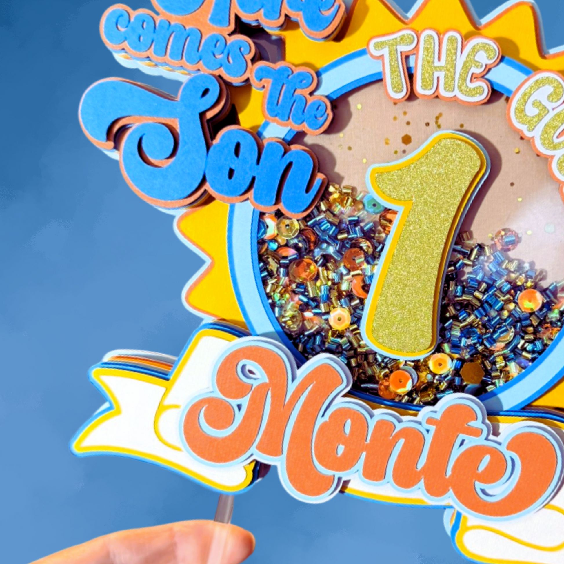 Decorative birthday cake topper with colorful text and number '1' against a blue background