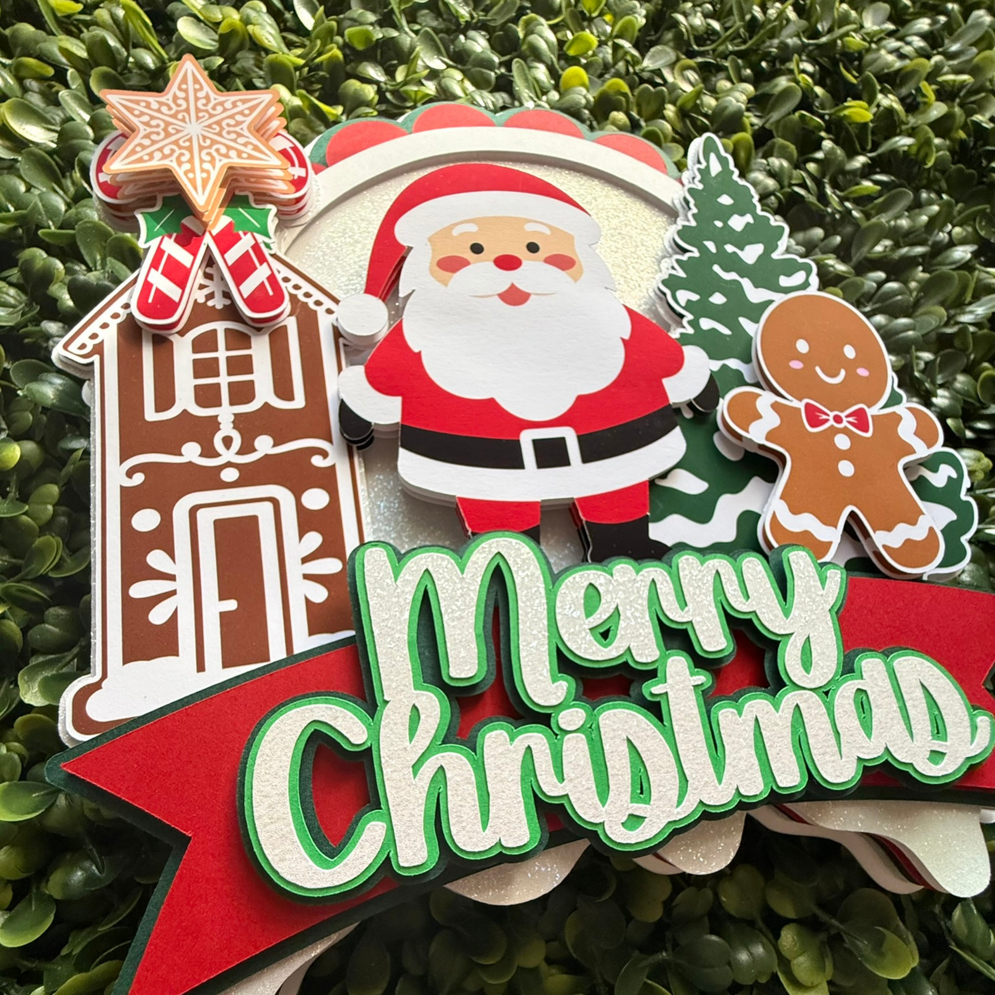 Decorative Christmas cake topper with Santa Claus, gingerbread house, and tree on a green leaf background.