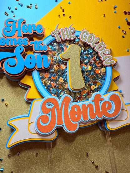 Decorative birthday sign with 'Here comes the son' and 'The golden 1 Monte' text on a colorful background.