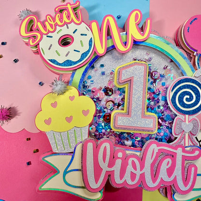 Decorative birthday cake topper with colorful text and graphics for a first sweet birthday celebration.